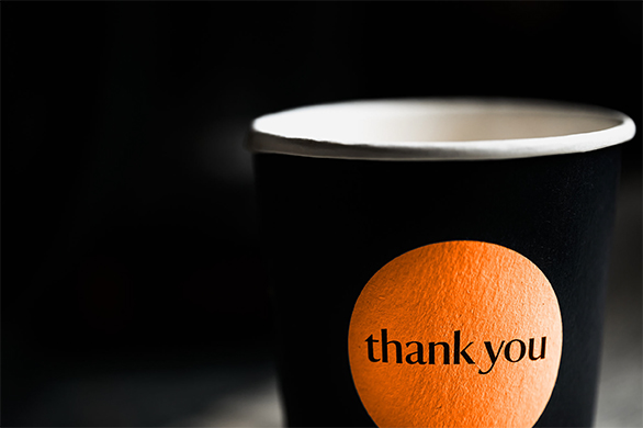 Image of a black cup with an orange circle featuring the words “thank you.”